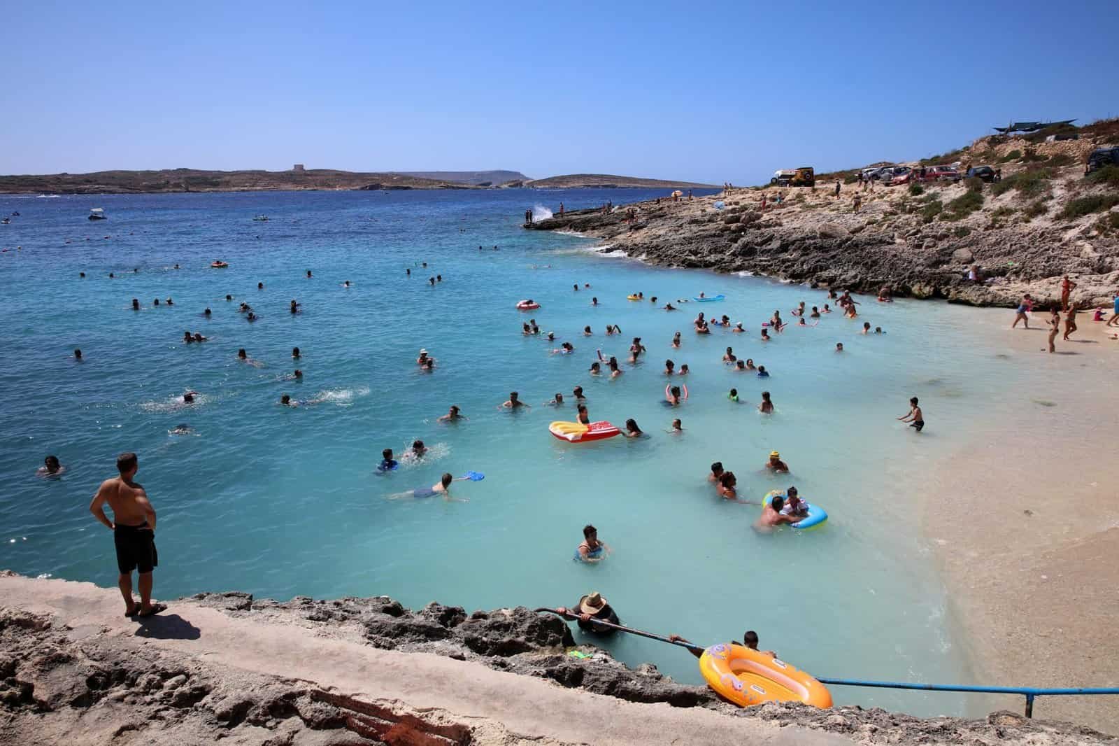 Groups of people swimming or standing in the sea, close to a sandy shore.