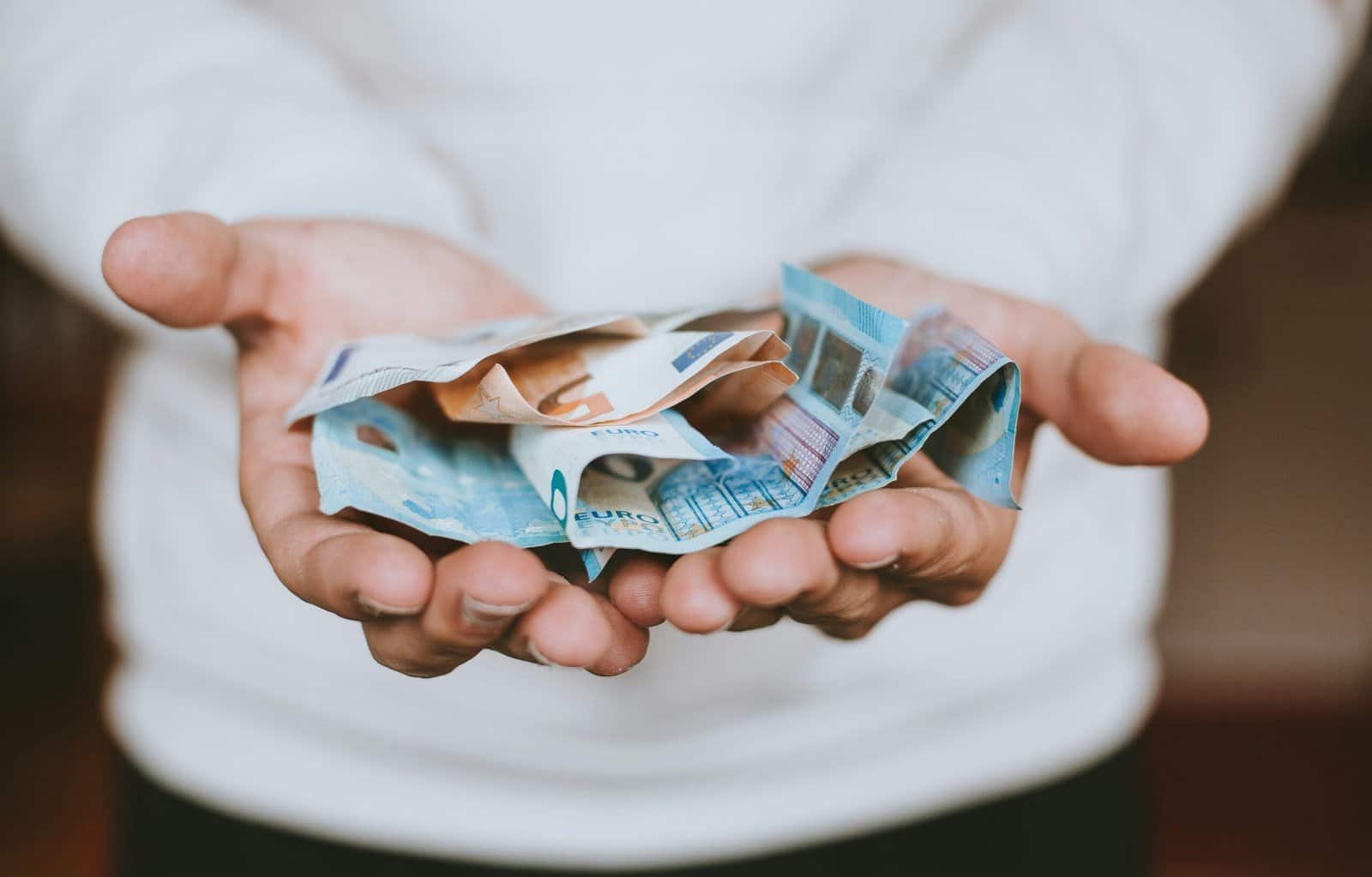 Two open hands holding several lightly folded Euro banknotes.