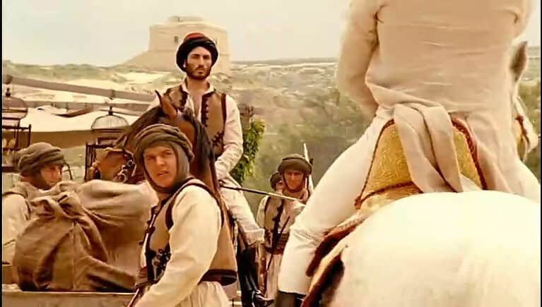 Two men on horsebacak face each other in a barren landscape.