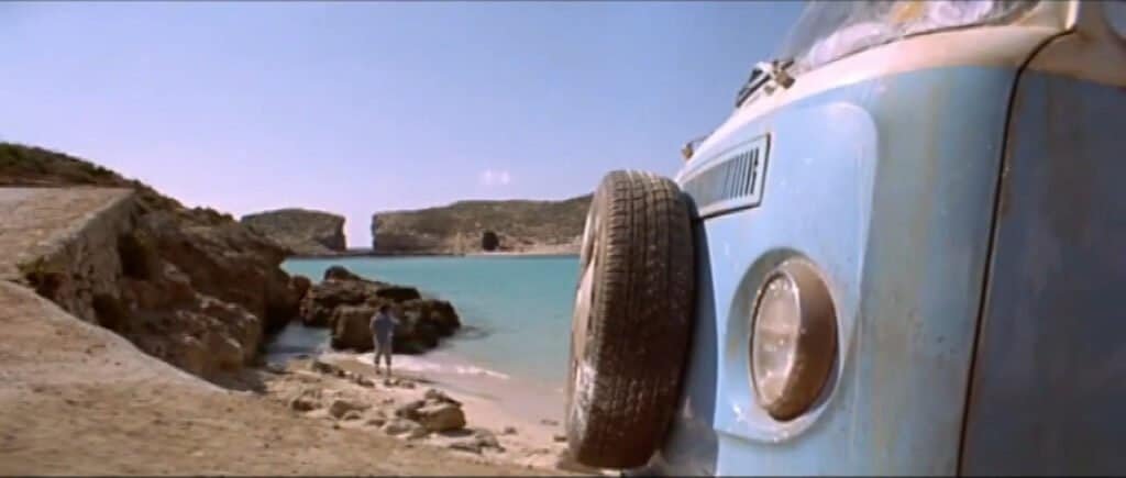 The back end of a light-blue, classic VW camper van on the beach at the Blue Lagoon, Comino.