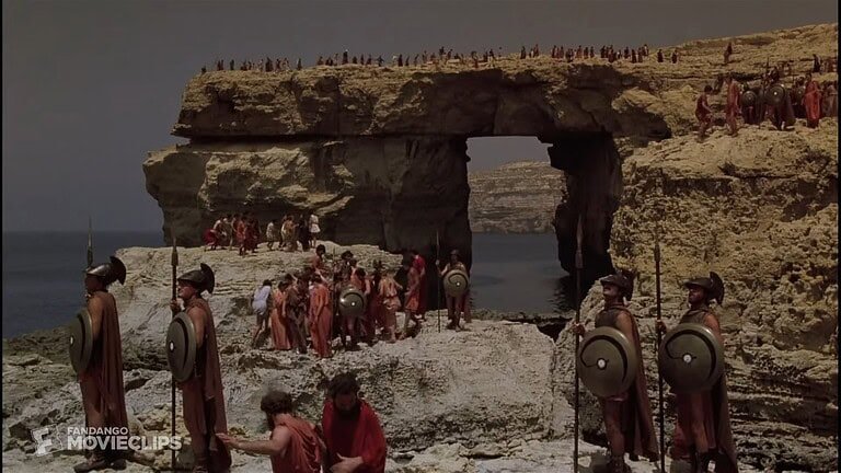 A group of people, dressed as ancient greeks, are gathered in front of the Azure window.