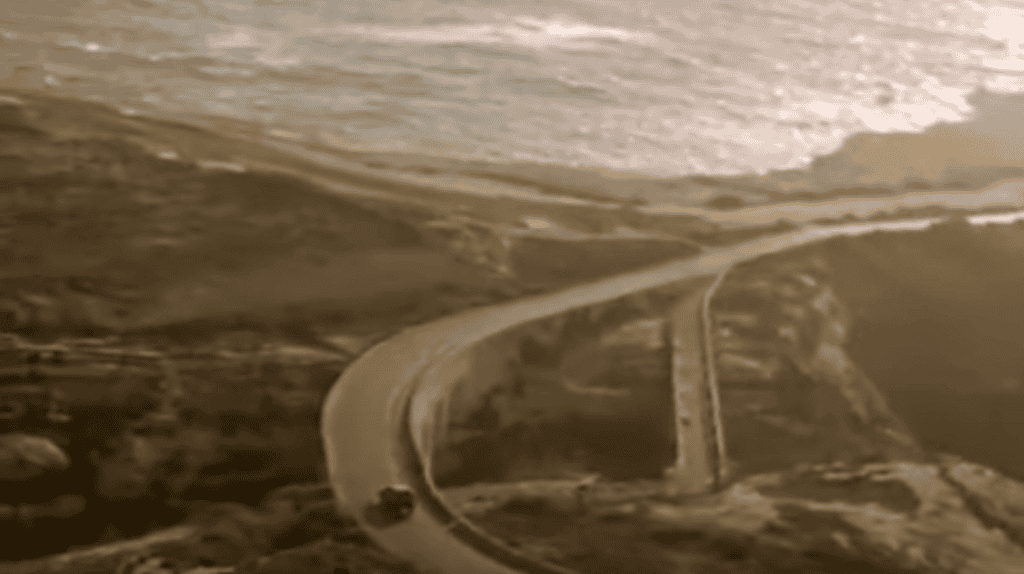 A car drives down a winding road towards the sea.