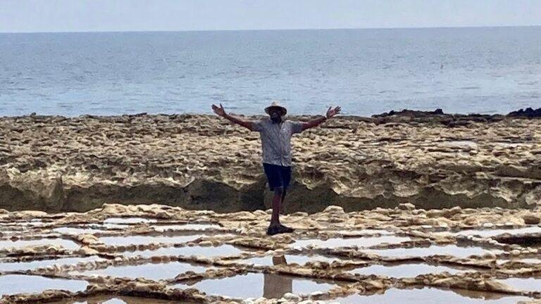 Ainsley Harriott stands with his arms spread wide in the middle of the Xwejni Salt Pans.