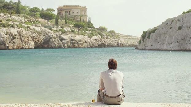Brad Pitt sits on the edge of a quay, looking at Mgarr Ix-Xini and the hotel from By The Sea.