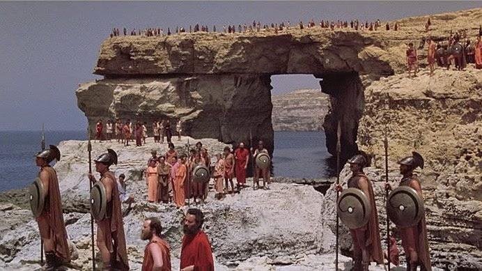 A group of people, dressed as ancient greeks, are gathered in front of the Azure window.
