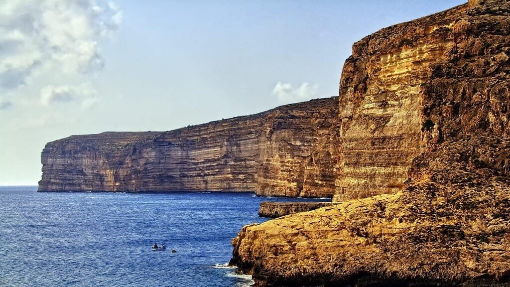 Sheer limestone cliffs framed by a calm sea and blue sky.