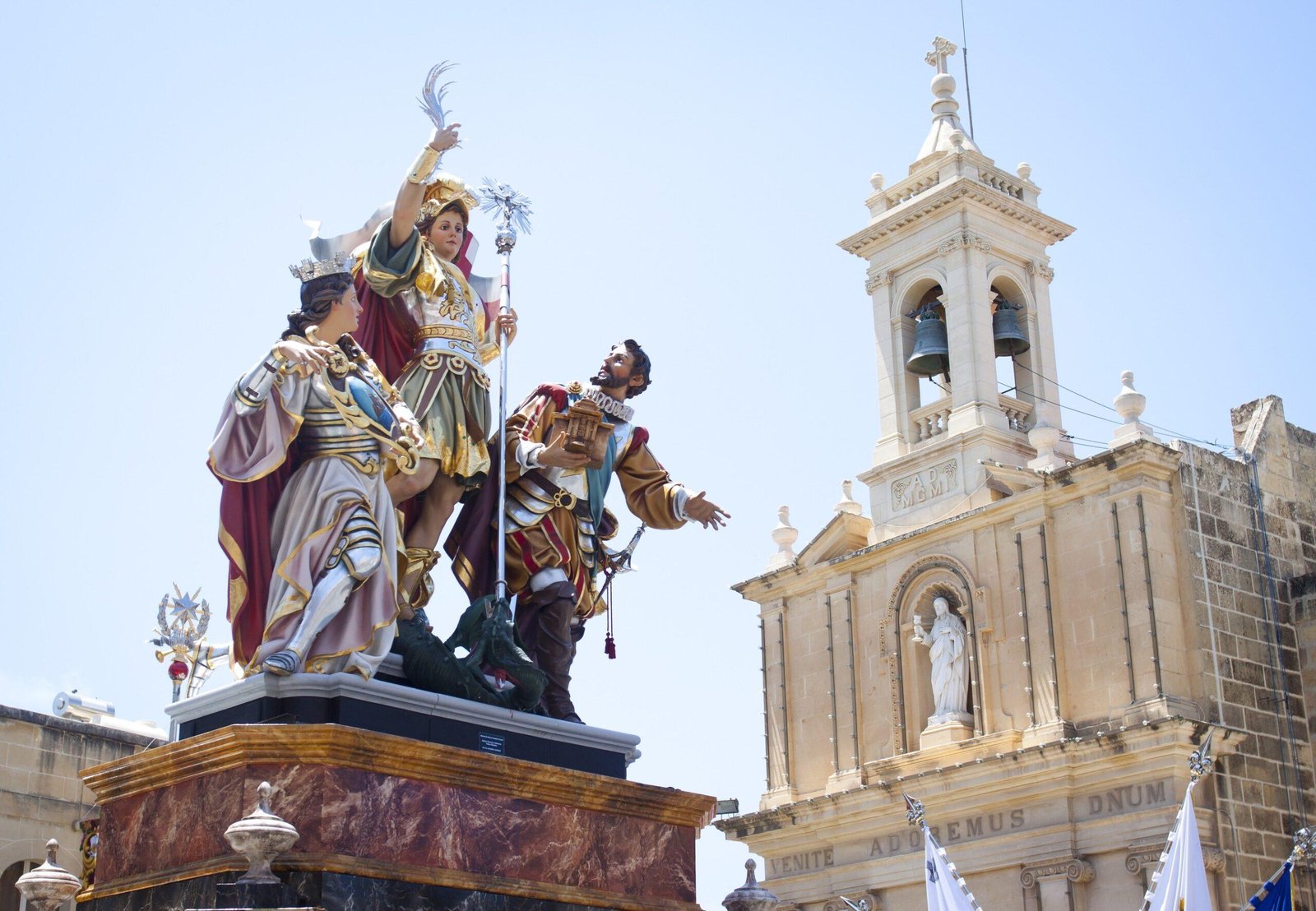 A statue of St George and two other figures is carried past a church.