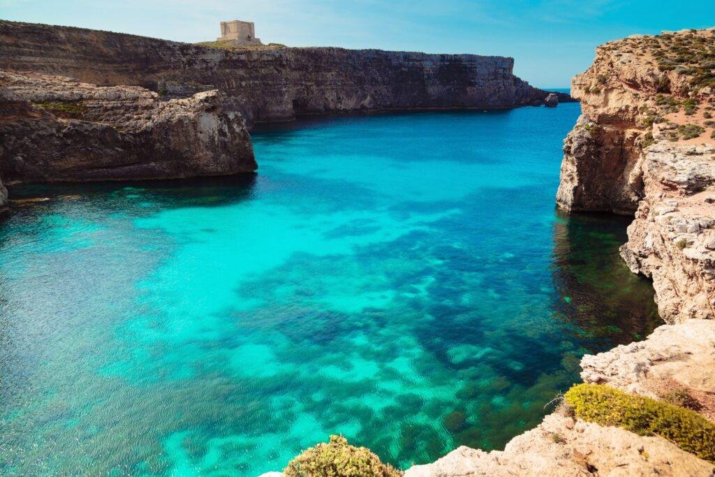 Mgarr Ix-Xini, Gozo. Crystal blue waters, lined by sheer limestone cliffs with Mgarr Ix-Xino tower visible on the farside.