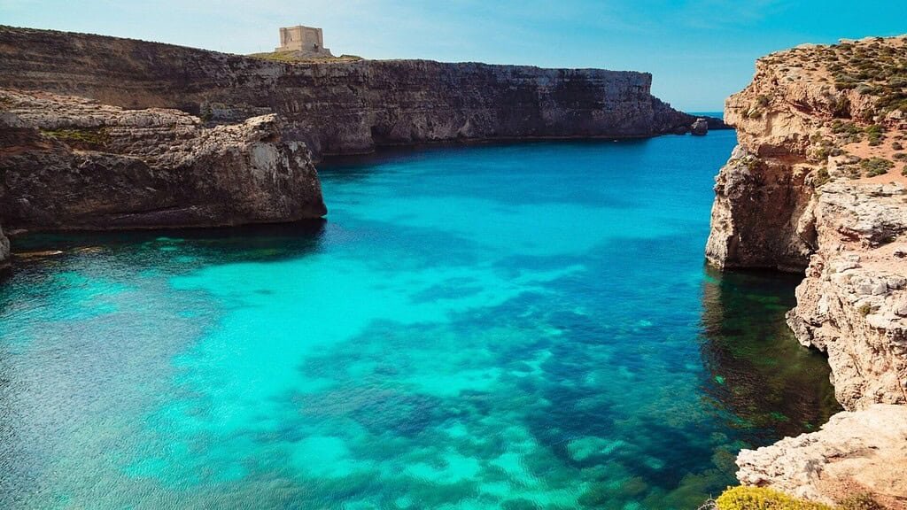 Mgarr Ix-Xini, Gozo. Crystal blue waters, lined by sheer limestone cliffs with Mgarr Ix-Xino tower visible on the farside.