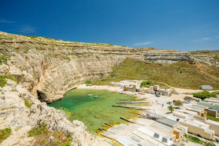 The Inland Sea, Dwerja. A shallow, semi-circle shaped, lagoon, surrounded by boathouses to one side and sheer cliffs to the other, with a cave leading to the sea.