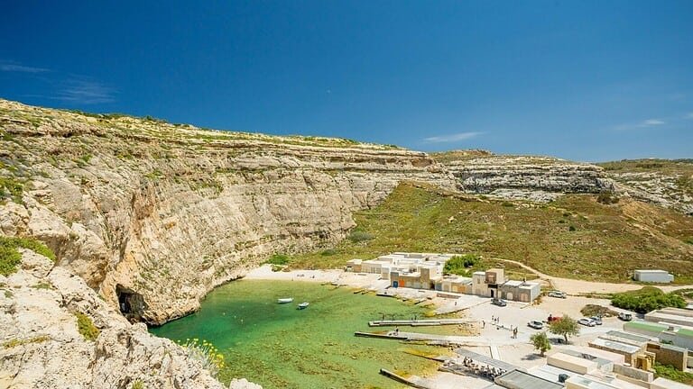 The Inland Sea, Dwerja. A shallow, semi-circle shaped, lagoon, surrounded by boathouses to one side and sheer cliffs to the other, with a cave leading to the sea.