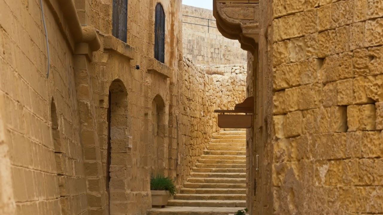 A cat sitting on a stone wall next to a staircase in Gozo's Citadel.