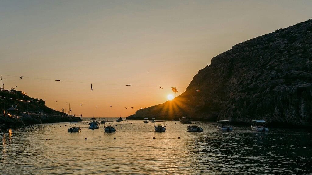 Xlendi Bay at sunset, with boats moored in the harbour.