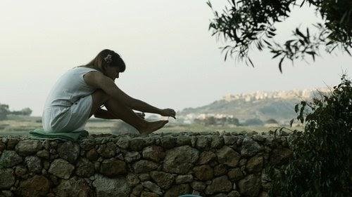 A woman sits on a limestone rubble wall, looking over a field.
