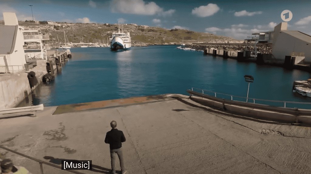 Matthias Koeberlin, as Hartwig Seeler, stands on the quay at Mgarr Harbour, watching the Gozo Channel Ferry approach.
