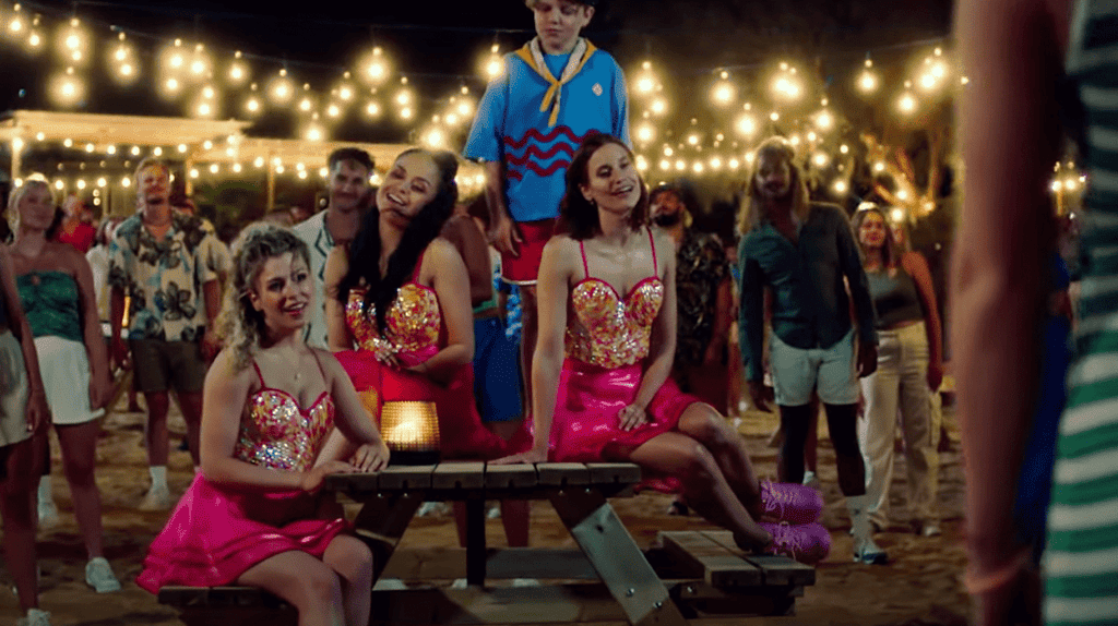 The group K3 sit on a picnic table surrounded by party goers.