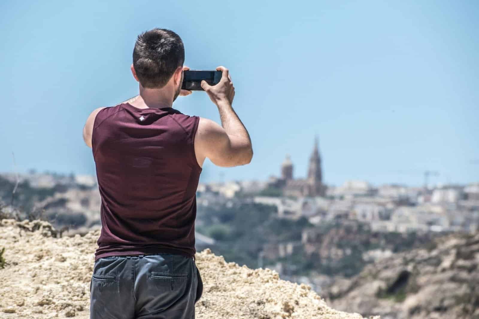 A man takes a photo on a smartphone of ghajnsielem Church.