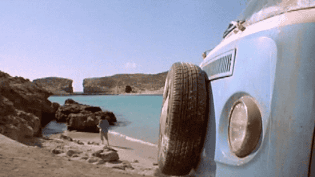 The back end of a light-blue, classic VW camper van on the beach at the Blue Lagoon, Comino.