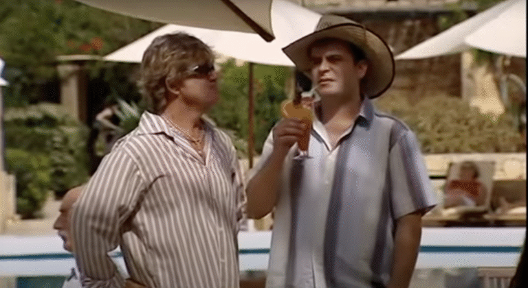 Two men, dressed in short sleeve shirts, have a conversation by a hotel pool