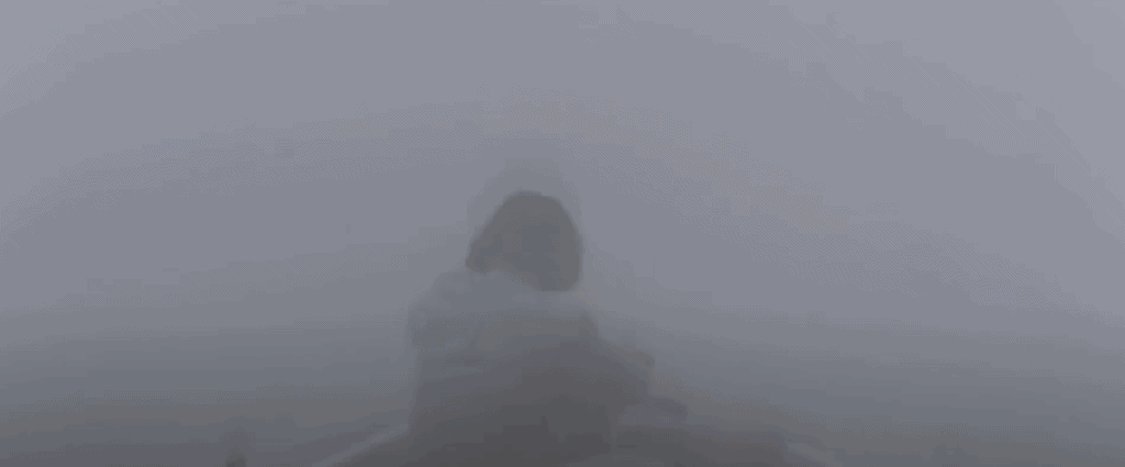 A figure looks out from a boat deck, surrounded by mist.