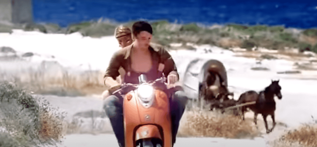 A man and woman on a scooter being followed by a horse and cart.