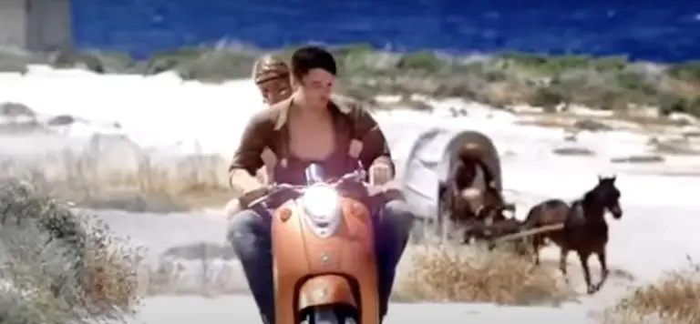 A man and woman on a scooter being followed by a horse and cart.