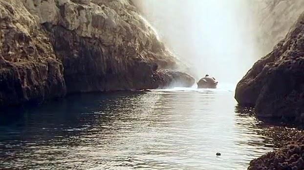 A diving bell surfaces next to a sheer cliff.