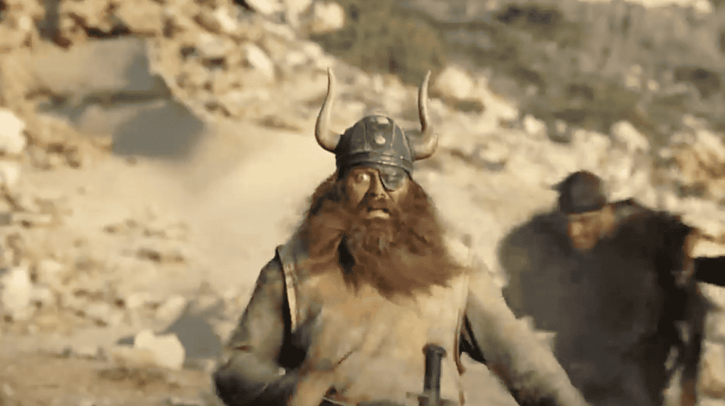 A man dressed as a Viking, with a big beard and eye patch, runs down a hill towards the camera.