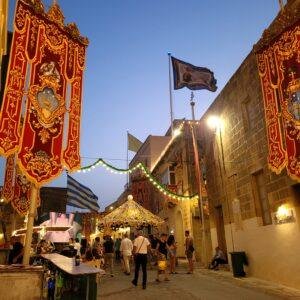 A Gozo street decorated with Festa banners and flags, filled with people