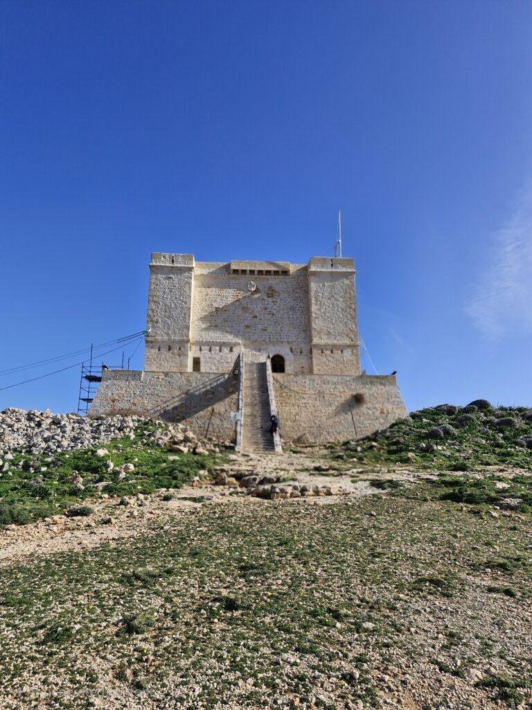 A square limestone tower with steep steps leading up to it.