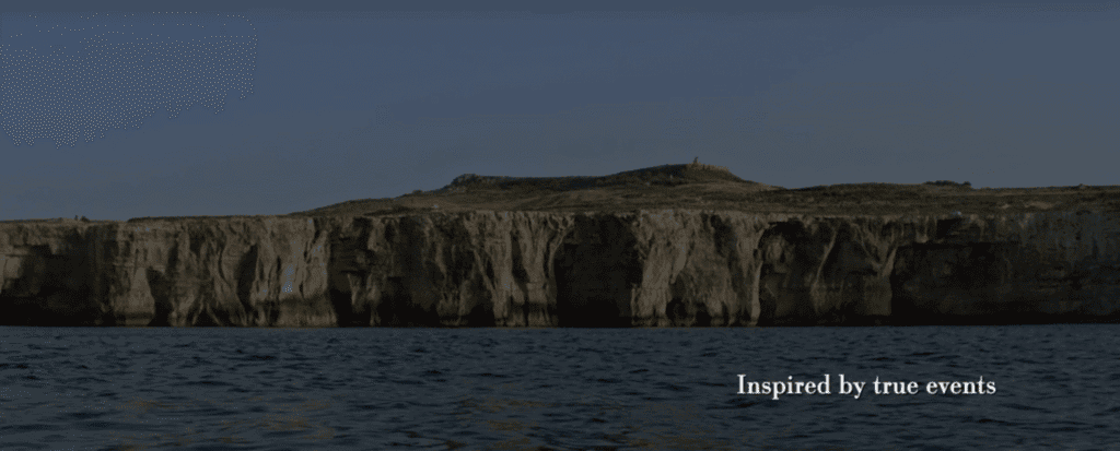 Sheer limestone cliffs tower above a calm blue sea.
