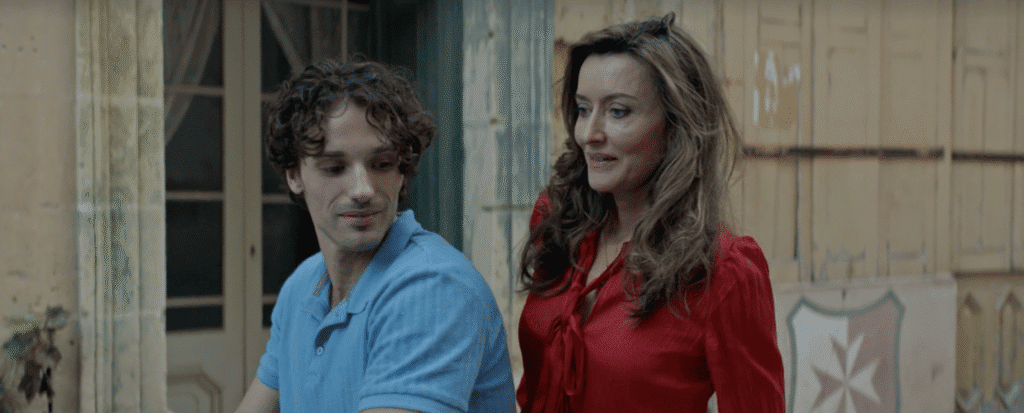 A young male and female sit on a scooter outside an old building.