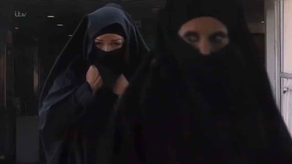 Two figures in black burhkas walking.