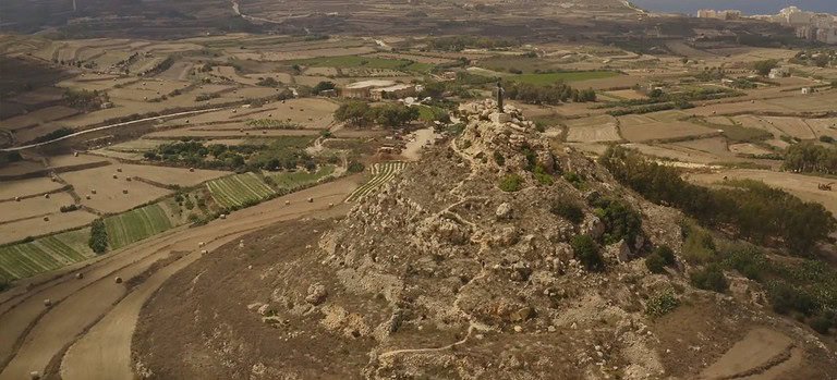 An aerial view of two men climbing a limestone mound. At the top there is a statue that is similar to Christ the Redeemer in Brazil.