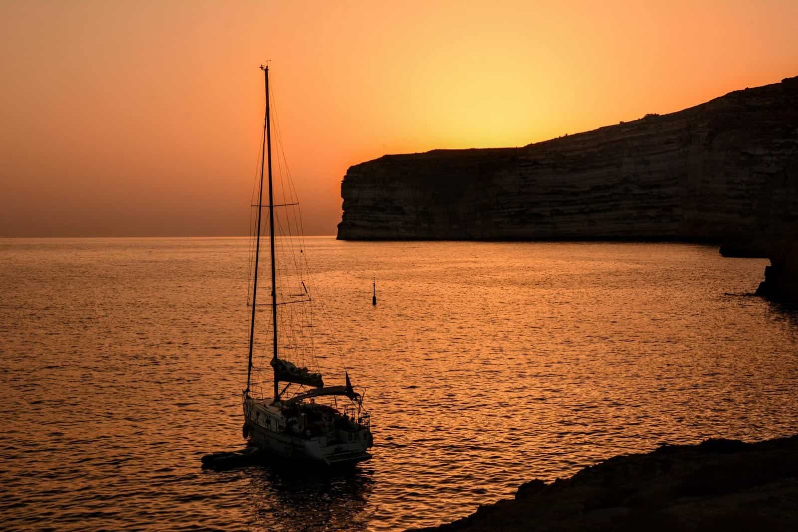 A sailboat anchored in quiet waters during a stunning sunset in Malta, capturing serene golden hour beauty.