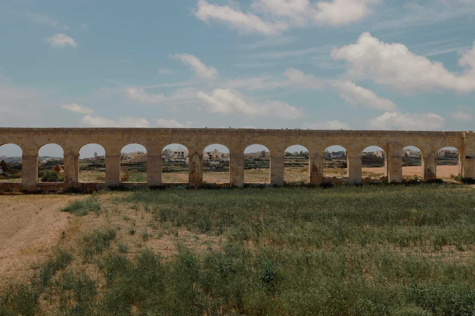 A scenic view of the ancient Gozo aqueduct in Malta, framed by fields and a clear sky.