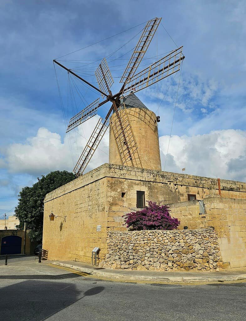 A scenic view of the historic Ta' Kola Windmill located in Xaghra, Malta, under a blue sky.