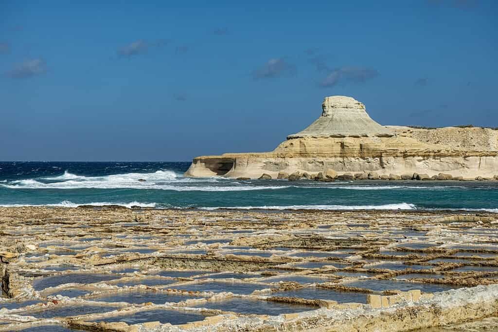 Dramatic seascape with salt pans and rocky coastline in Malta under clear blue skies.