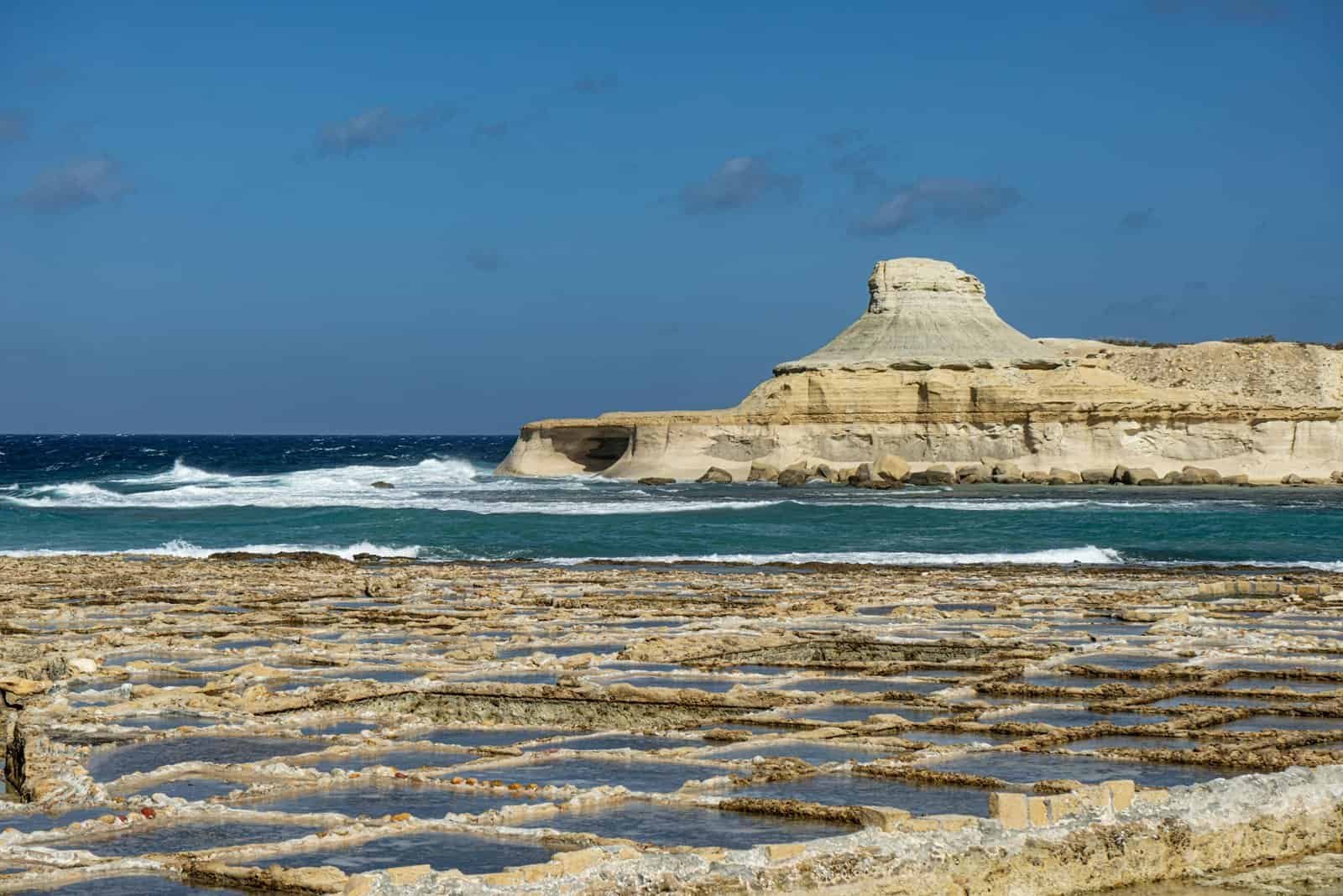 Dramatic seascape with salt pans and rocky coastline in Malta under clear blue skies.