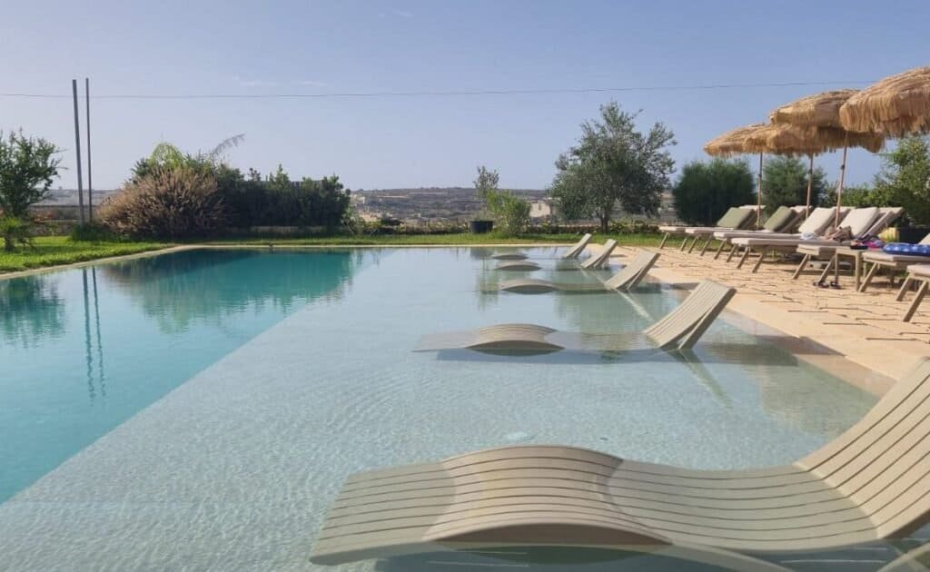 Tuta Agrotourism's outdoor pool, a large rectangular pool with a shallow shelf to the right, with semi-submerged loungers.