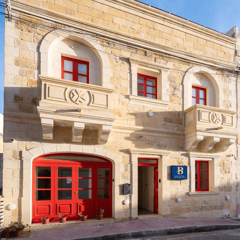 The frontage of Battistini Boutique Living and Spa, a traditional limestone building with red painted windows and doors with carved balconies. 
