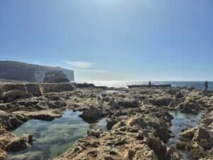 Rocky coastline of Gozo with clear tidal pools and sea views under bright sunlight.