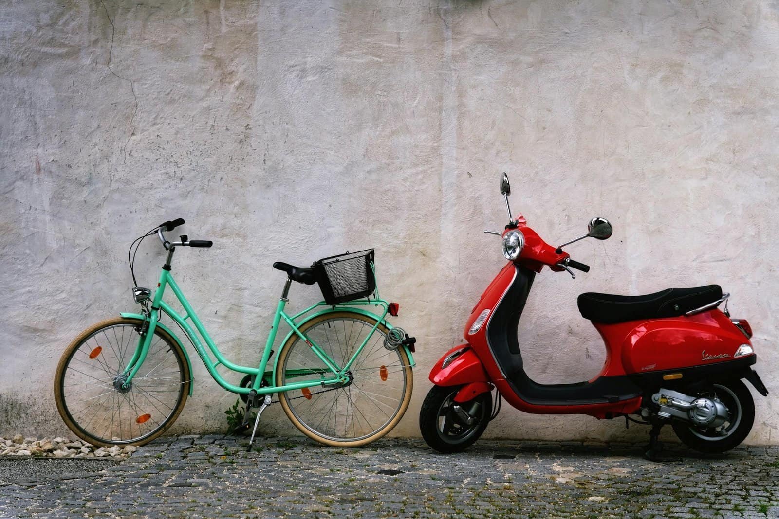 Parked bicycle and scooter side by side in front of a rustic wall, showcasing urban transportation options.