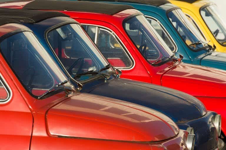 Row of vintage cars with vivid colors parked in sunlight, showcasing retro design.