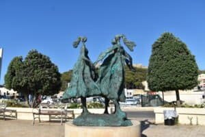 Bronze statue of two dancers in Gozo's outdoor square under clear blue sky.