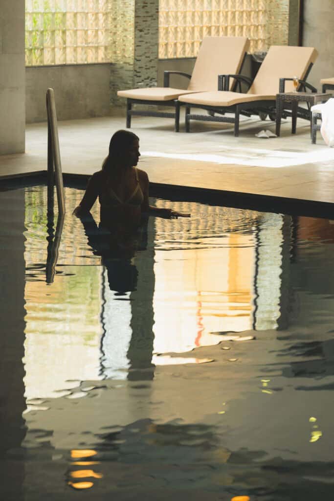A woman wading into the indoor pool at the Grand Hotel's ELEMIS Spa, Għajnsielem, Gozo, with loungers behind