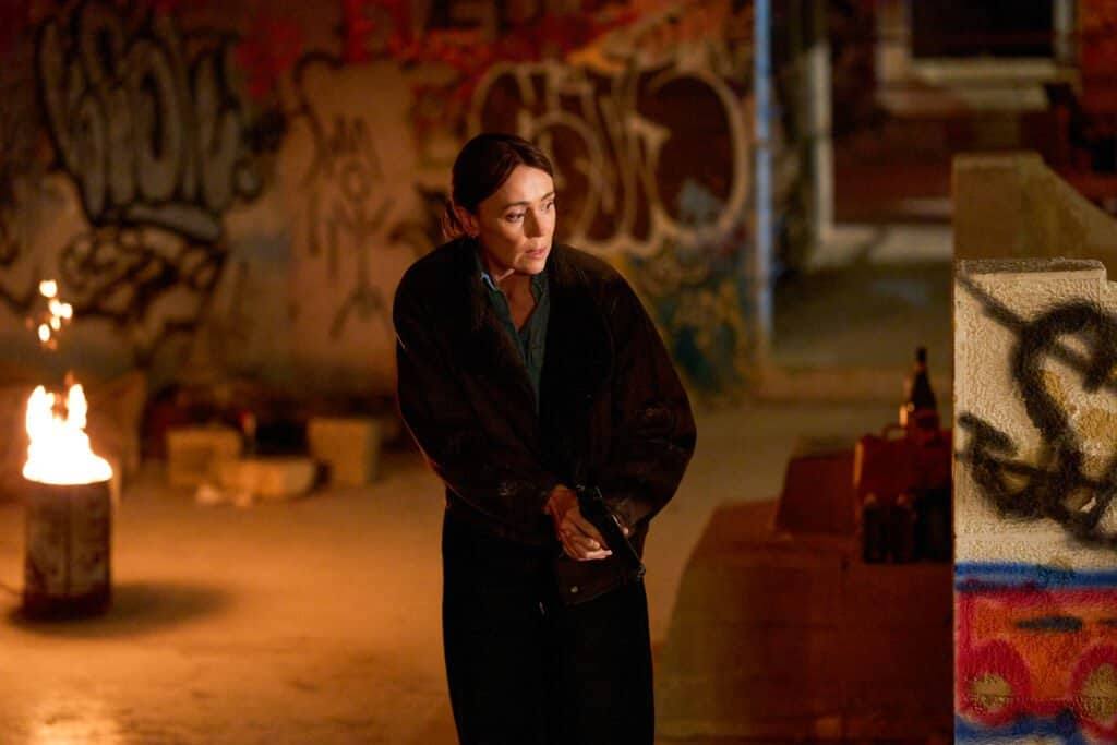 Keeley Hawes as Julie holding a gun in a graffiti-covered building at night in The Assassin series 2