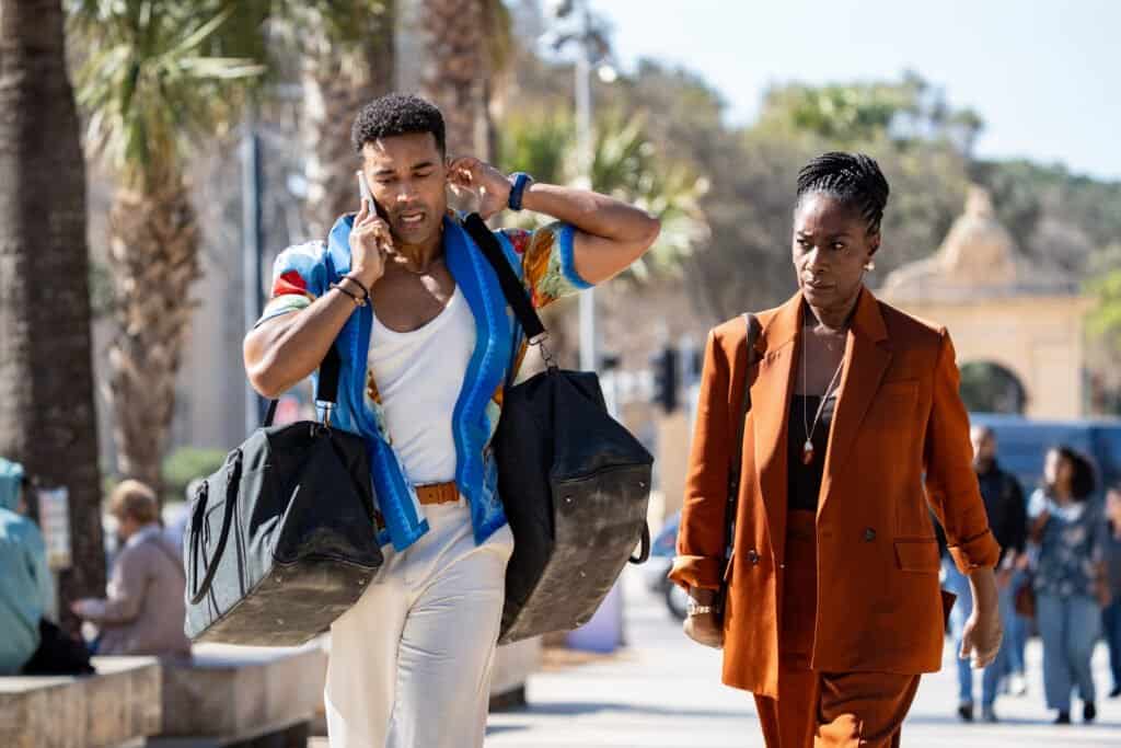 Devon Terrell and Jacqueline Boatswain as Ezra and Isha walking along a palm-lined street in The Assassin series 2