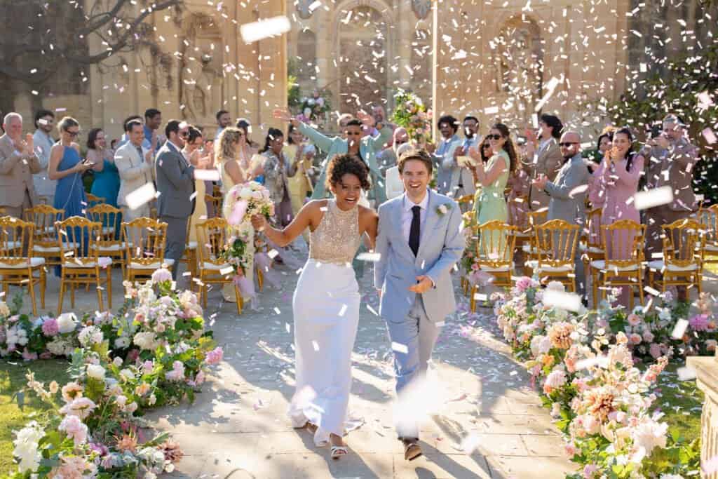 Kayla and Edward walk through confetti at their wedding in the gardens of Villa Bologna, Attard, in The Assassin